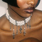 Close-up of a woman wearing a pearl necklace with cross pendants against a neutral background