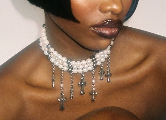 Close-up of a woman wearing a pearl necklace with cross pendants against a neutral background