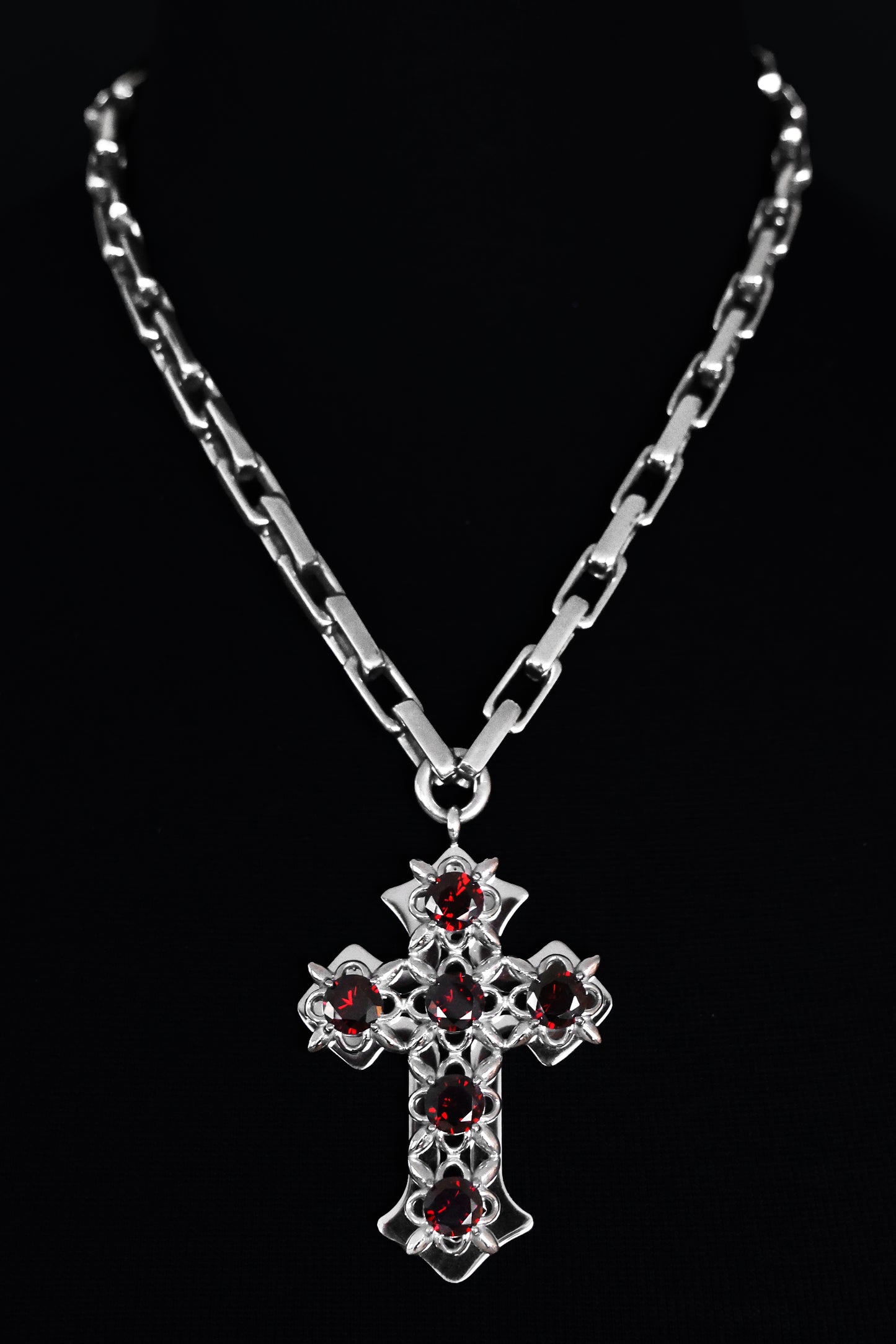 Stainless steel cross necklace with red stones on a black background.