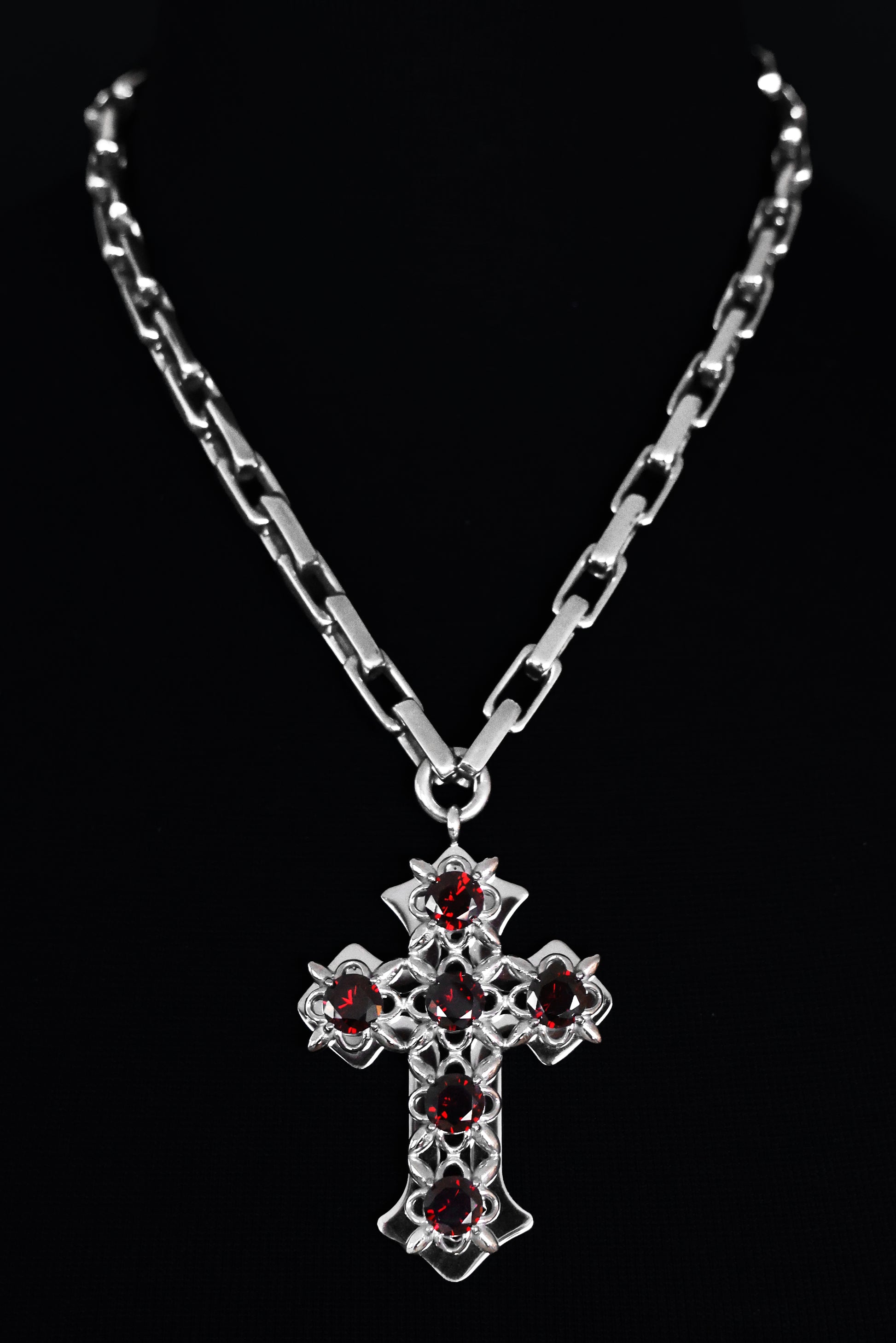 Stainless steel cross necklace with red stones on a black background.